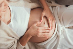 Lovely mum making heart shape by hands over stomach