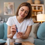 Blood sugar testing at home. Checking Blood Sugar Level At Home. Diabetic Checking Blood Sugar Levels. Woman checking blood sugar level by glucometer and test stripe at home