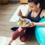 Sporty young woman eating healthy while listening to music sitti